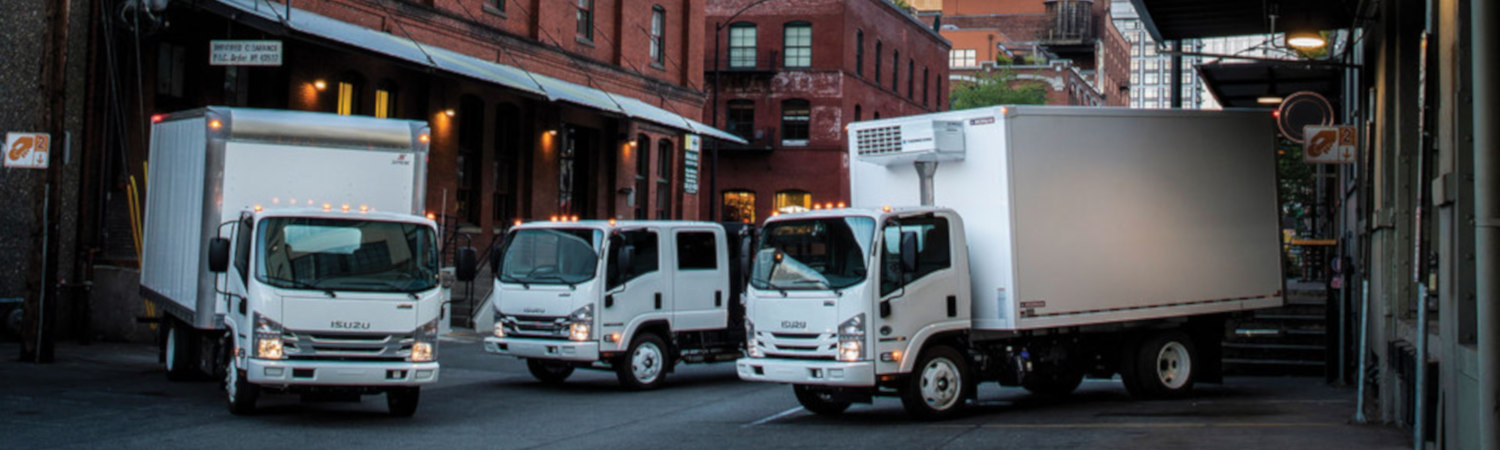 Three 2020 Isuzu trucks station themselves for delivery in a narrow city street.
